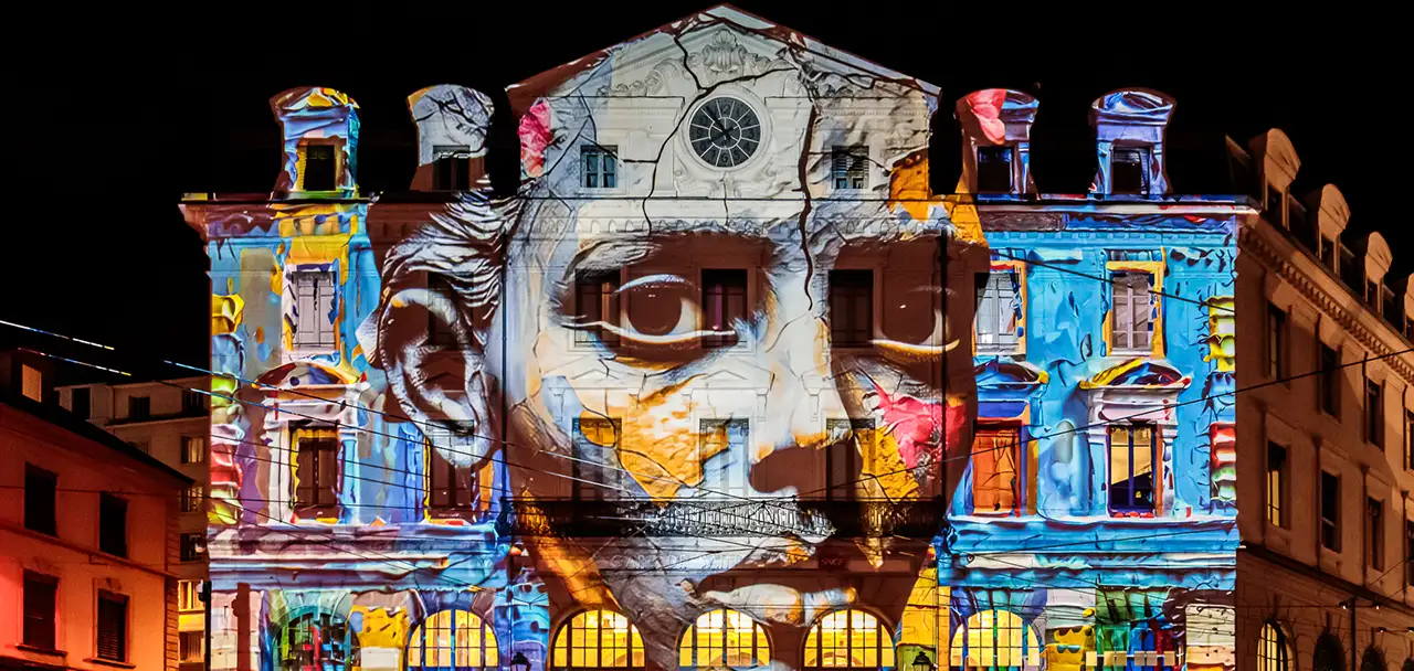 La façade d’un bâtiment transformée par une projection lumineuse colorée formant un immense visage aux yeux intenses.